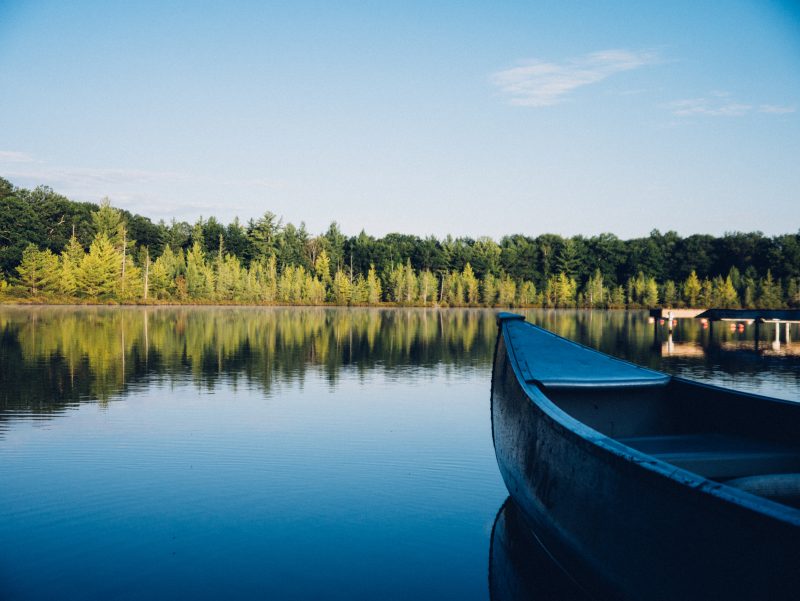 canoe on a lake with forest and clear blue sky