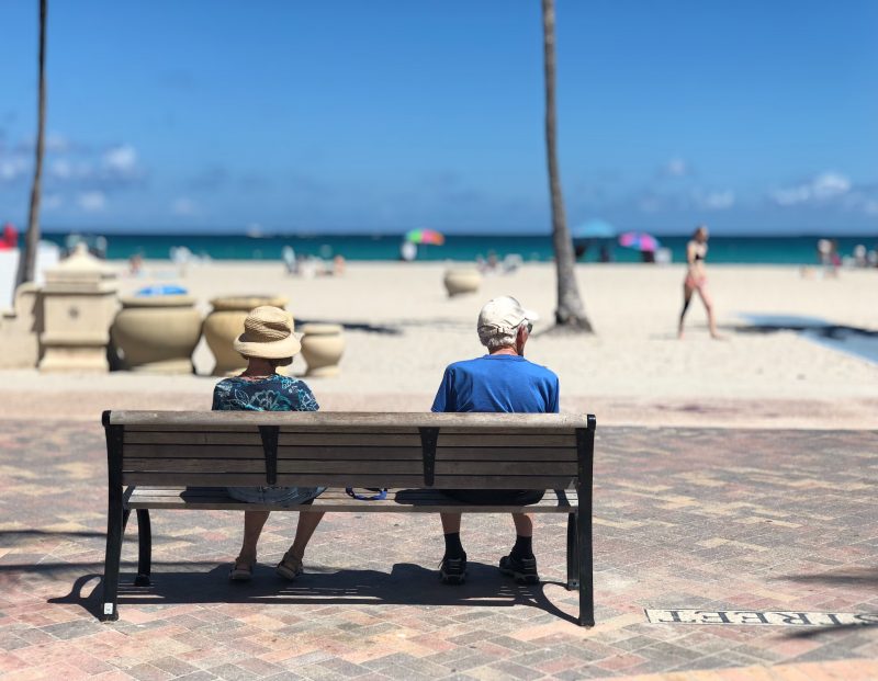 two elder people sitting on a bench by the beach