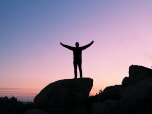 person on a rock with a purple sunset