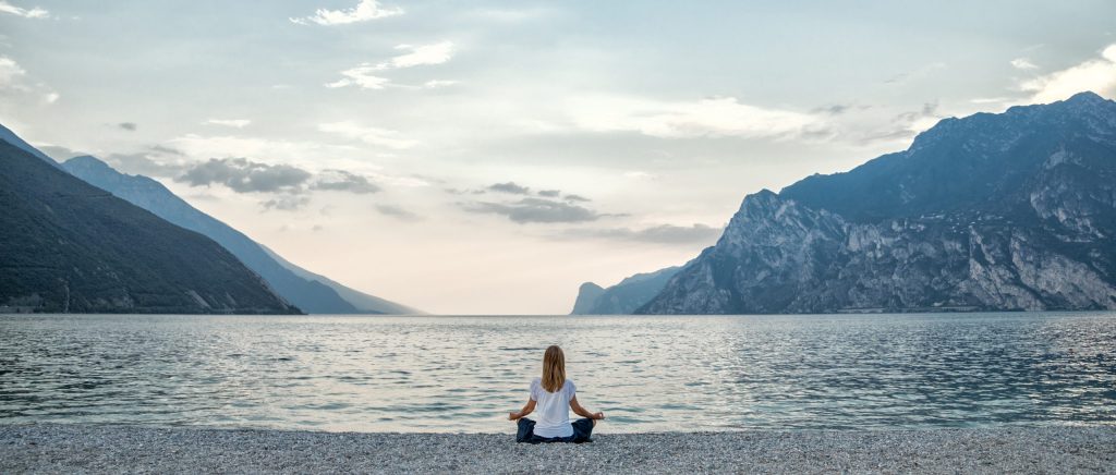 Woman meditating with a lake and mountains in the background