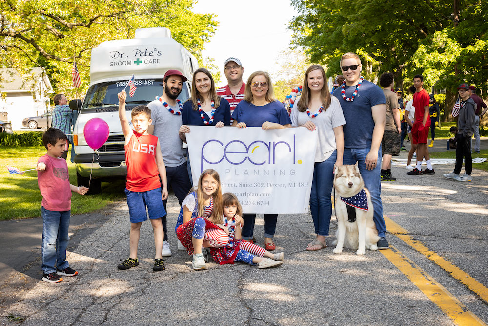 Team members of Pearl Planning and their families holding a Pearl Planning banner at a parade in Dexter Michigan