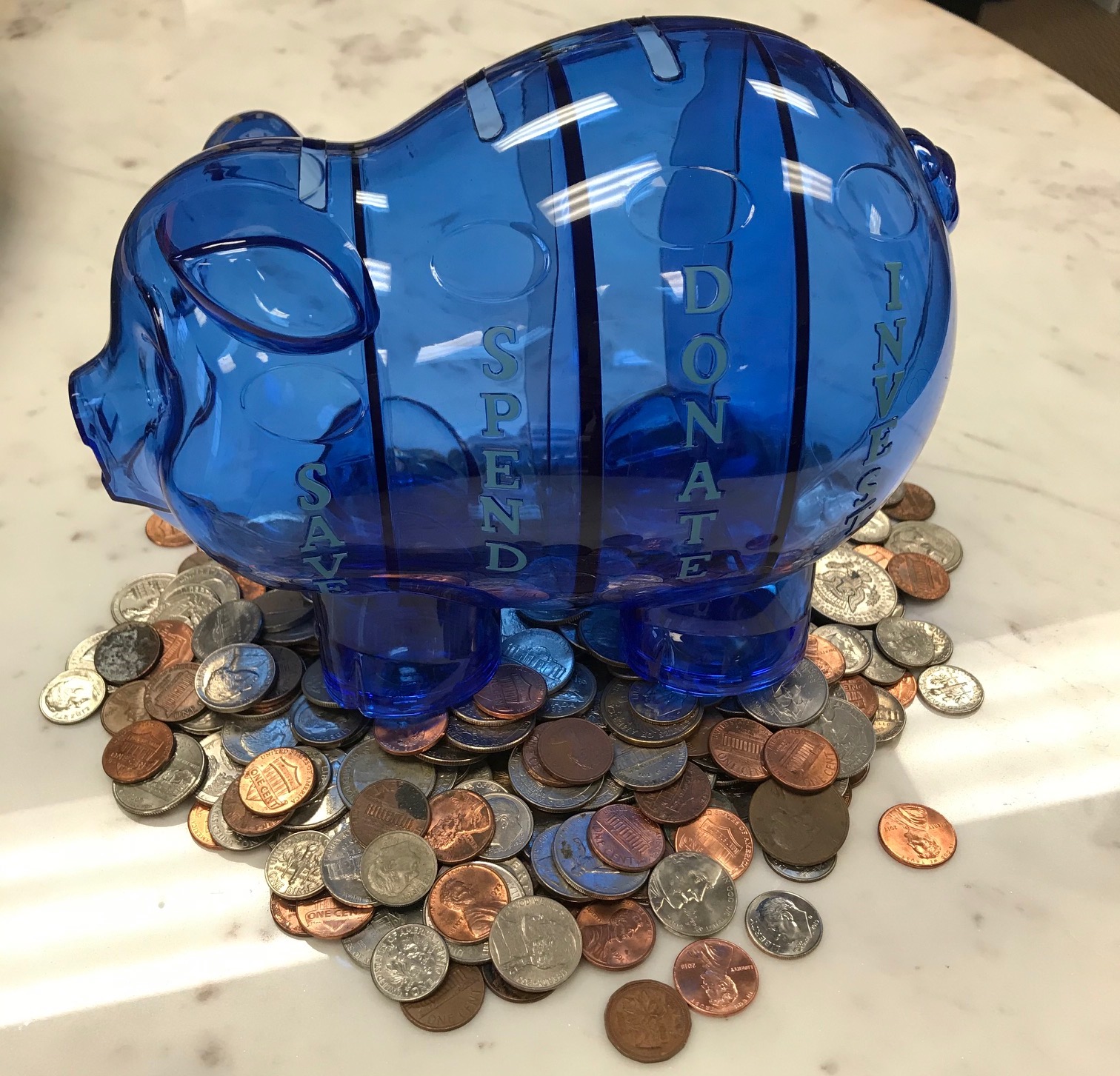 Blue see-through piggy bank with lots of change in front of it