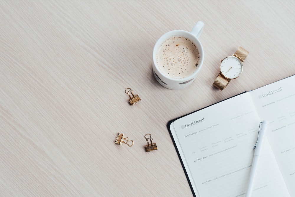 goal planner on a desk with coffee, watch, and clips