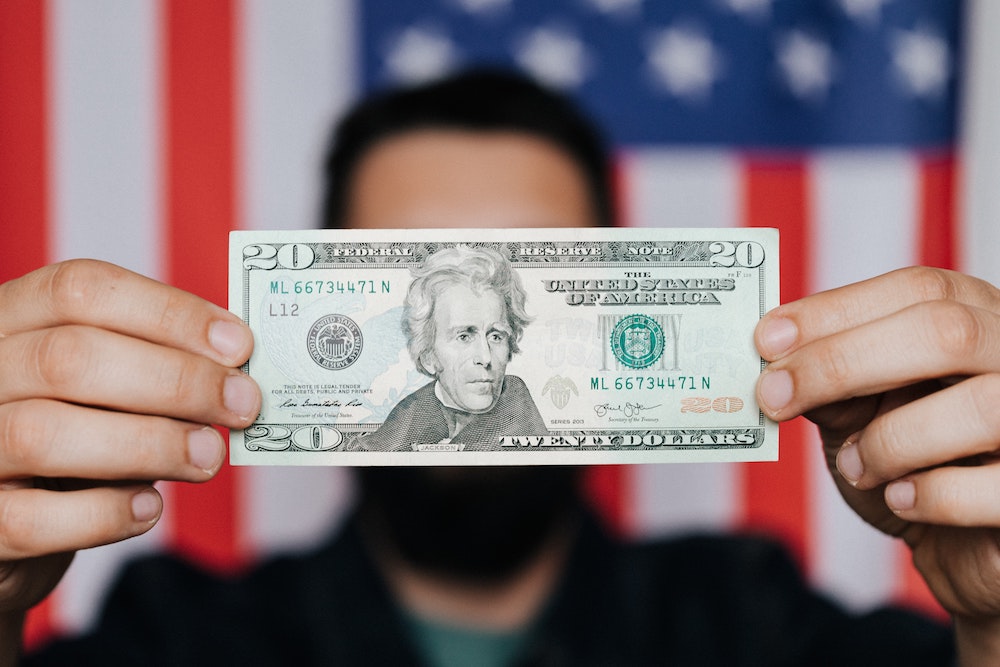 person holding a dollar bill with the american flag in the background