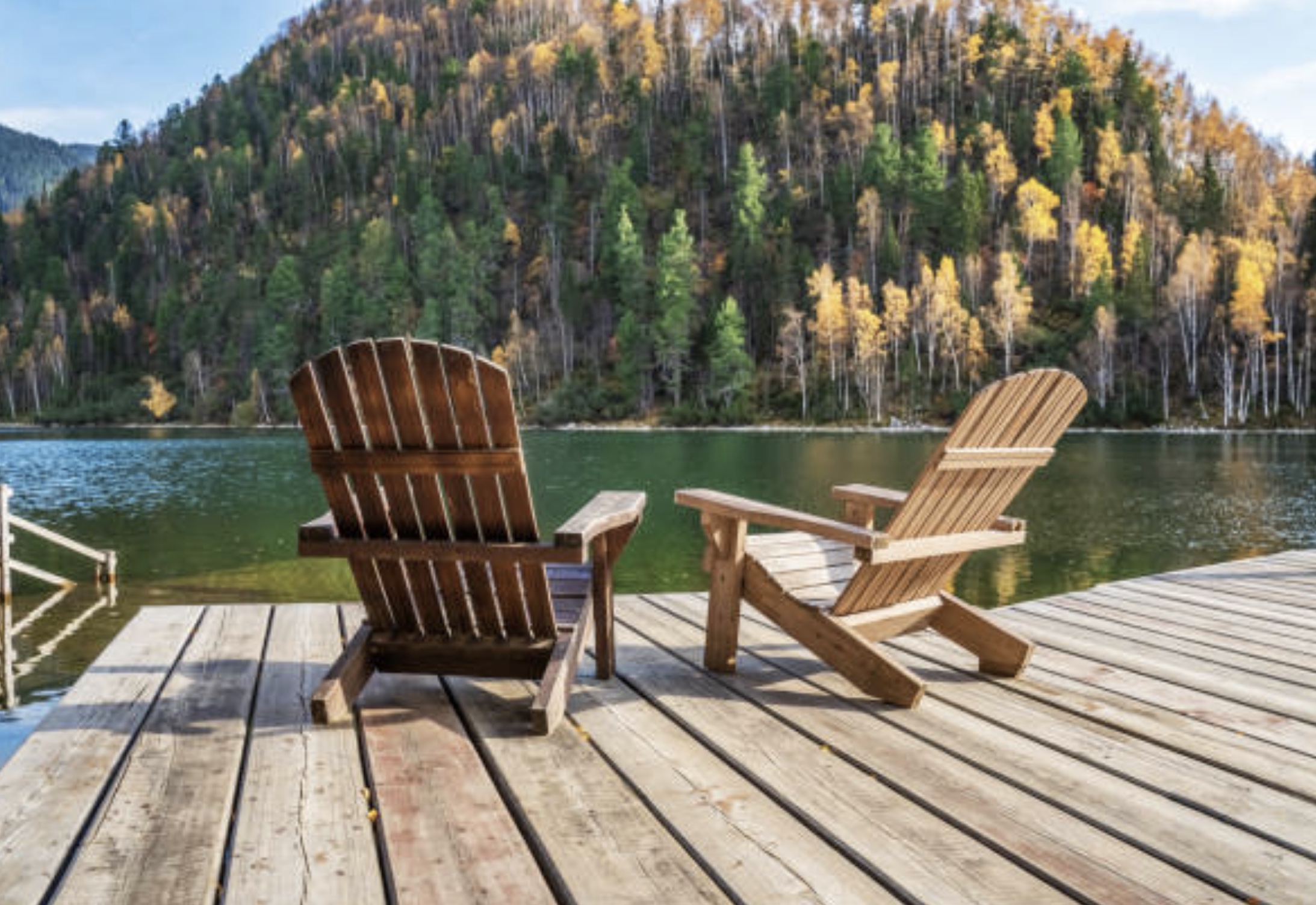 two adirondack chairs on a dock looking out at the lake